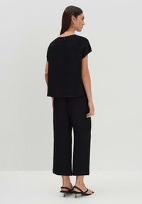 Top nero con texture, maniche corte e dettaglio a chiave sulla schiena, abbinato a pantaloni neri a gamba larga. Silhouette complessiva rilassata e morbida.