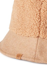 Béžový klobouk s širokým okrajem vyrobený z texturovaného fleecu, hladkým filcovým lemem a malým koženým detailem s logem. Měkký, teplý materiál.