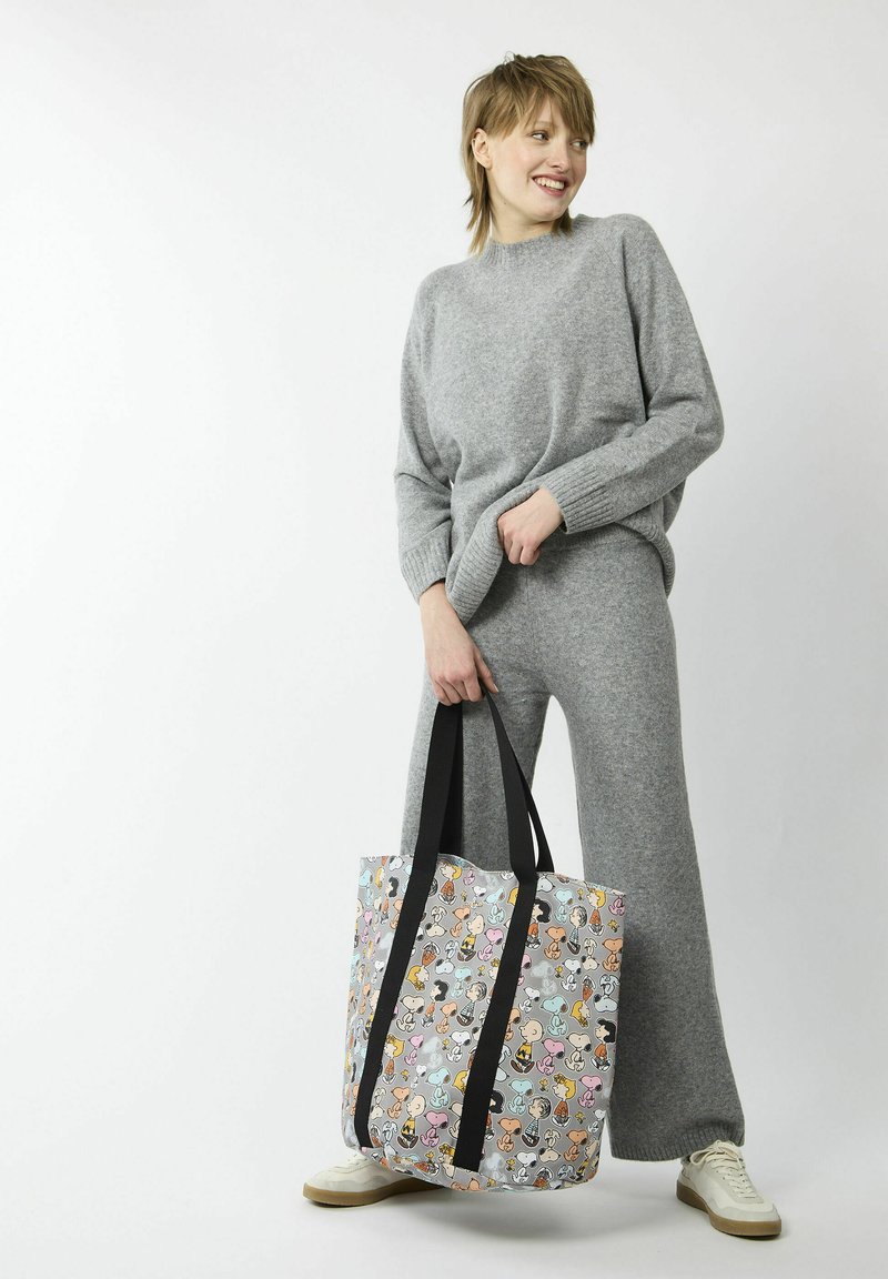 Grauer Strickpullover und passende weit geschnittene Hosen. Große Tote-Tasche mit einem bunten, cartoonartigen Tiermuster und schwarzen Trägern. Weiße Sneaker.