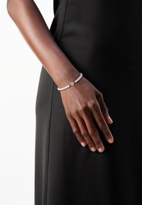 Pulsera de perlas con un acento central de diamante. Perlas blancas distribuidas de manera uniforme, con un acabado suave y brillante. Lleva puesta en una muñeca esbelta.