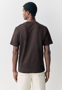 T-shirt en coton marron avec une coupe décontractée, manches courtes et col rond. Texture lisse avec des détails de coutures minimalistes.