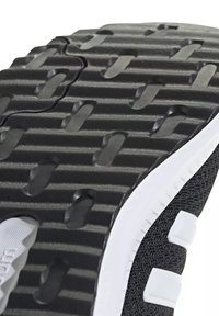 Gros plan de la semelle noire et blanche d'une basket avec un motif de bande de roulement texturé et une partie de la tige en mesh noir de la chaussure visible.