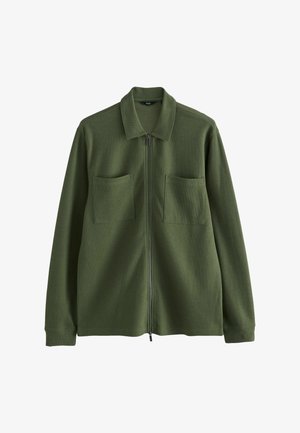 Veste zippée verte avec col, deux poches poitrine et une finition en tissu texturé. Manches longues avec poignets côtelés.