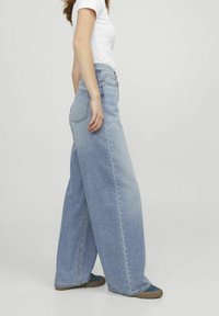 Bredbenta blå denimjeans med blekt utseende, hög midja och två bakfickor. Bärs med en åtsittande vit t-shirt och avslappnade skor.