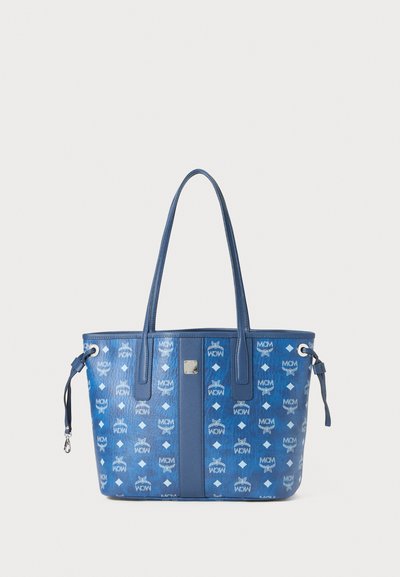 Niebieska torba na ramię z błyszczącą teksturą, z powtarzającym się wzorem logo MCM, dwiema solidnymi uchwytami i srebrnymi akcentami metalowymi.