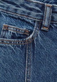 Jean en denim bleu foncé, avec une poche, des coutures orange et une texture de tissu lisse. Gros plan sur les coutures et les détails.