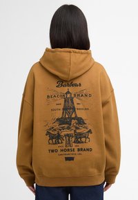 Καφέ φούτερ με ευρύ πανί, διαθέτει μαύρη γραφική εκτύπωση ενός φάρου, αλόγων και κειμένου στην πλάτη. Μαλακό, υφασμάτινο ύφασμα.