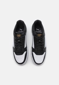 Sneaker bianco e nero con tomaia in pelle e mesh, caratterizzati da una punta perforata, chiusura con lacci e dettagli dorati sulla linguetta.