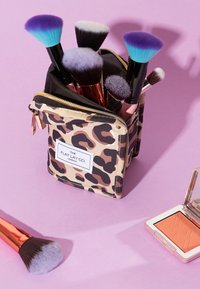 Support de pinceaux de maquillage avec un design à imprimé léopard. Il contient divers pinceaux aux poils colorés et un blush compact.