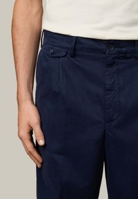 Marineblauwe broek van een gladde stof, met een voorvaksluiting met knopen, zijzakken en een vlakke voorkant met een subtiele glans.