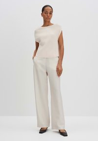 Top in maglia beige chiaro con una vestibilità rilassata, abbinato a pantaloni crema a gamba larga e décolleté neri appuntiti, che mostrano un look minimalista.