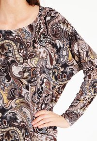Długi rękaw bluzki z wzorem paisley w kolorach brązowym, kremowym i czarnym. Wykonana z miękkiego materiału, z okrągłym dekoltem i luźnym krojem.
