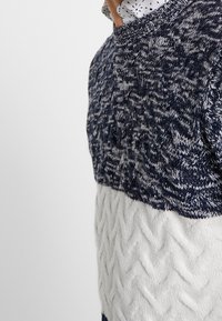 Stickad tröja med en färgblockdesign i marinblått och vitt. Texturerad övre del med ett vågmönster och kabelstickade detaljer på den nedre delen.