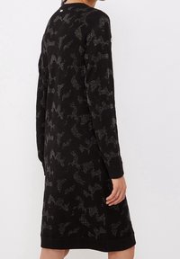 Svart klänning med ett texturerat mönster och silverfärgad detalj, långa ärmar, rundad halsringning och en avkopplad passform som slutar under knäna.