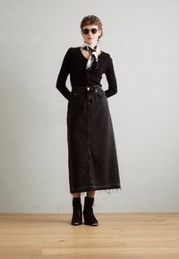 Fustă maxi din denim negru cu margine desfăcută, asortată cu un top negru mulat și un fular alb-negru. Model care poartă ochelari de soare închiși la culoare.