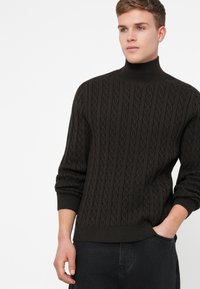 Dunkelbrauner Rollkragenpullover mit strukturiertem Zopfmuster und gerippten Bündchen. Lässige Passform mit einem einfarbigen Bund.