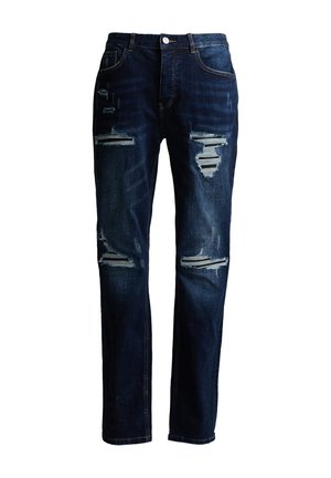 Tmavomodré úzke džínsy s viacerými horizontálnymi trhlinami a strapcami na predných stehnách a kolenách, zapínanie na gombík a zips.