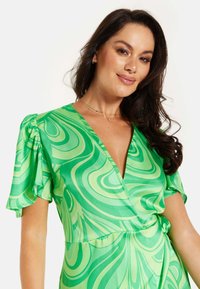 Green dress with a wrap design, featuring a swirling pattern in varying shades of green. Short puffed sleeves and a deep V-neckline.