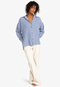 Light blue button-up shirt with a textured fabric and long sleeves, paired with cream wide-leg pants. The shirt has a collar and front buttons.