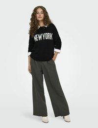 Maglione nero a maglia con "NEW YORK" in lettere bianche, abbinato a pantaloni a vita alta di un verde scuro a gamba larga e stivali alla caviglia beige con tacco.