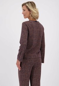 Getextureerde gebreide top in paarse en bruine tinten, met lange mouwen en een ronde halslijn. Kenmerkt een knoopdetail aan de achterkant voor sluiting.