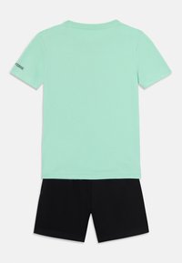 Camiseta de algodón de color verde menta con mangas cortas y cuello redondo, combinada con pantalones cortos de algodón negros, que tienen bolsillos laterales.