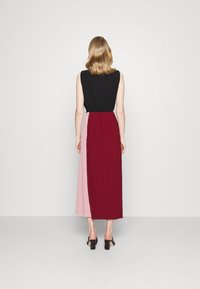 Robe Maxi avec un haut noir ajusté et une jupe bicolore comportant des panneaux bordeaux et rose pastel. Texture lisse et design longueur cheville.