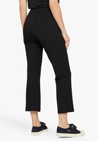 Zwarte, strakke broeken met een gladde textuur, cropped lengte en hoge taille. Gecombineerd met donkere sneakers met witte zolen en strikaccenten.