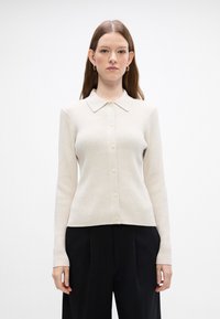 Lys beige ribbet cardigan med krage, lange ermer og knappestilling. Har et teksturert stoff og subtil glans.