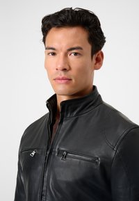 Schwarze Lederjacke mit hohem Kragen, ausgestattet mit zwei Reißverschlusstaschen auf der Brust, glatter Textur und subtilen Steppnähten.