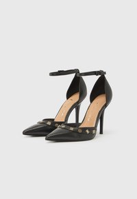 Μαύρα δερμάτινα ψηλοτάκουνα παπούτσια με μυτερές μύτες, λουράκια αστραγάλου και διακοσμητικές χρυσές λεπτομέρειες κατά μήκος του μπροστινού μέρους. Ομαλή υφή.