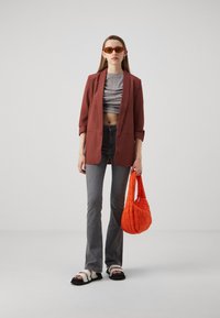 Blazer rouge sur un crop top côtelé gris, jeans évasés gris, sandales blanches et noires, et un sac à main matelassé orange.