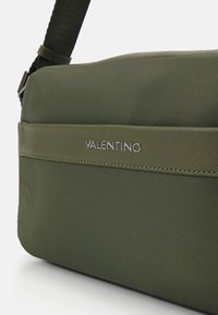 Valentino grønn nylon skulderveske med flat design, som har en fremtredende merkevarelogo og justerbar stropp i matchende materiale.