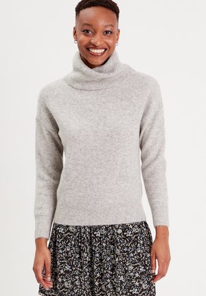 Hellgrauer Rollkragenpullover mit geripptem Saum und Bündchen. Weiche Textur, lockere Passform, getragen über einem gemusterten Blumenkleid.