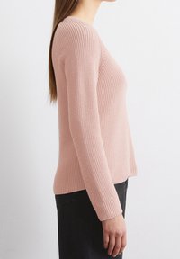 Pull en maille côtelée rose clair, à manches longues, au design ajusté et à la finition texturée, présenté en vue de profil.