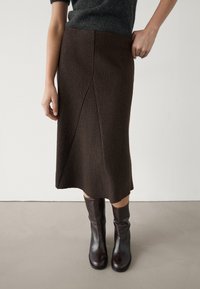 Ruuskean polvipituisen hameen, joka on valmistettu tekstuurista kankaasta, sivusaumadetaileilla, yhdistelmä ruskeiden nahkasaappaiden kanssa, jotka ovat polvisuunnassa.