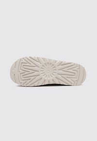 Semelle d'une chaussure beige présentant un motif de semelle en explosion de soleil avec des rainures en zigzag et un petit logo circulaire au centre.
