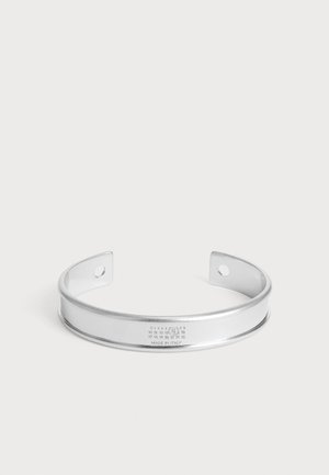 Srebrna metalowa bransoletka mankietowa z dwoma otworami na końcach oraz małymi wygrawerowanymi liczbami i tekstem "Made in Italy" z przodu.