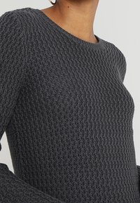 Grijze gebreide trui met een textuur patroon, ronde halslijn en lange mouwen met een lichte flare bij de manchetten.
