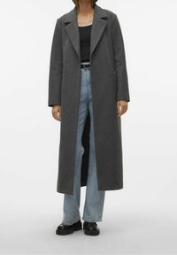 Grå uld lang frakke med klapper og frontlommer, iført over en sort top og blå slidte jeans, parret med sorte platform sko.