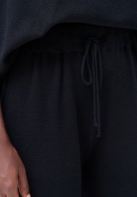 Zwart gebreide loungewear met een gestructureerde stof, elastische tailleband met trekkoord en een losse pasvorm rond de onderkant.