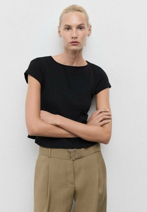 Haut noir ajusté à manches courtes, col rond, porté avec un pantalon taille haute kaki avec un détail de boucle en argent.