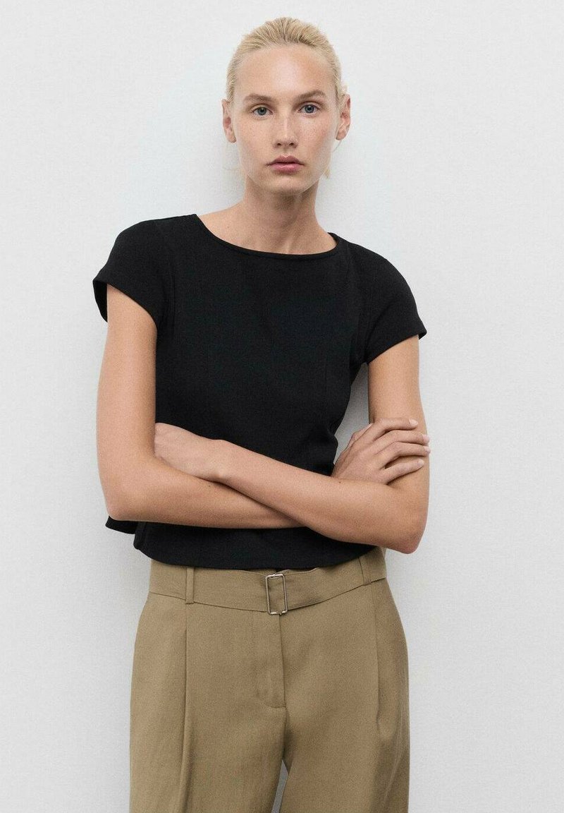 Black fitted top with short sleeves, round neckline, worn with khaki high-waisted trousers featuring a silver buckle detail.