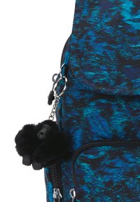 Zaino con tessuto testurizzato blu e nero, dotato di una tasca con zip e un portachiavi a pom-pom di pelliccia nera attaccato con una catena di metallo.