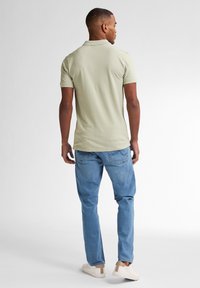 Polo shirt verde chiaro con maniche corte, abbinato a jeans blu e sneakers chiare; vestibilità casual e texture liscia.