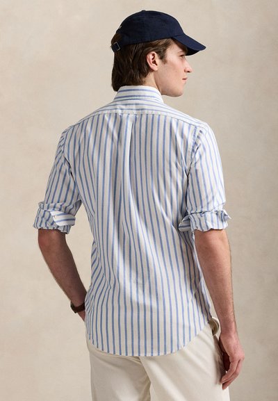 Košile na knoflíky s modrými a bílými svislými pruhy, dlouhými rukávy vyhrnutými na manžetách. Doplněná námořnickou čepicí.
