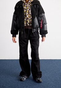 Schwarze Leder- und Kunstfell-Shortjacke, Hoodie mit Tiermuster, lockere schwarze Hose und graue Sneakers mit rosa Akzenten.