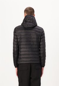 Giacca a vento nera con design trapuntato, cappuccio integrato e polsini elasticizzati, caratterizzata da una texture liscia e lucida.