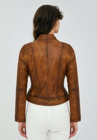 Bruine leren jas met een aansluitend ontwerp, zichtbare stiksels en een iets gestructureerd oppervlak. Beschikt over een kraag en lange mouwen.