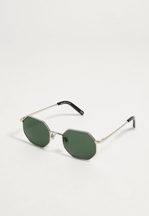 Lunettes de soleil octogonales avec fines montures en métal doré et verres vert foncé sur fond blanc.